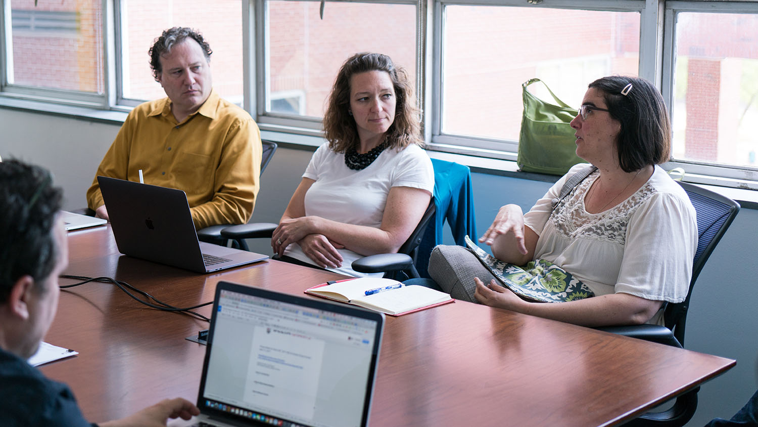 Three colleagues gathered with paper and laptops at a conference table.