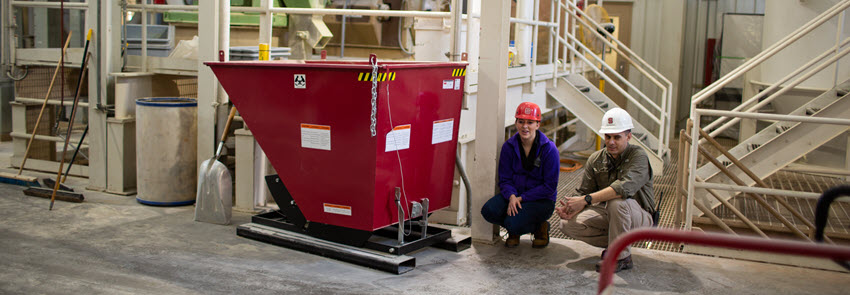 Two faculty members crouch down next to a red container at the feed mill.